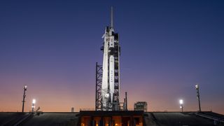 A black and white rocket stands on its launch pad with a purple twilight sky in the background