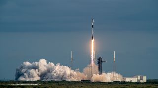 a black-and-white spacex falcon 9 rocket launches into a blue sky.