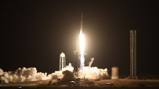 a rocket launches at night above a large plume of fire