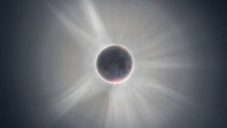 The moon's features are faintly visible. It is fully eclipsing the sun, which is hidden except for its corona glowing in white.