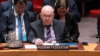 a man in a suit scowls while seated at a desk behind a sign that reads "Russian federation"