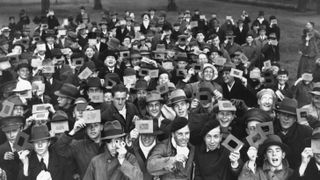 Lots of people with solar eclipse viewers looking up. The image is black and white.