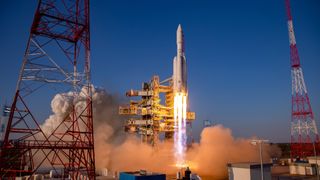 a large white rocket with four smaller boosters lifts off above a plume of fire