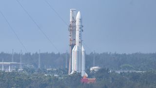 a large white rocket attached to a mobile tower rolls along a road surrounded by palm trees