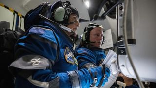 two astronauts with spacesuits on in a simulator looking at a screen