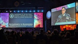 a man in a black military dress outfit gives a speech on a stage decorated with illuminated stars and planets