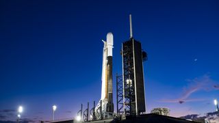 A white and black rocket on the launch pad with the crescent moon in the night sky