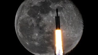 a silhouetted triple booster rocket passes in front of a full moon as fire spews from its engines.